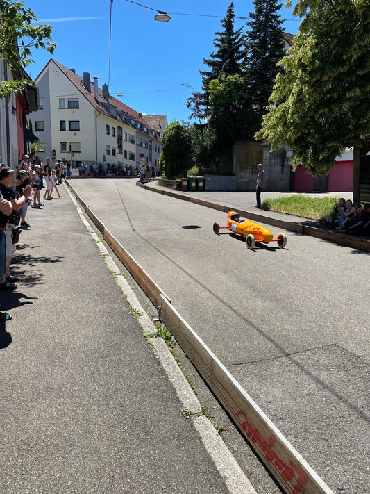 Kinder und Erwachsene bauen fröhlich gemeinsam eine Seifenkiste in einer hellen Werkstatt